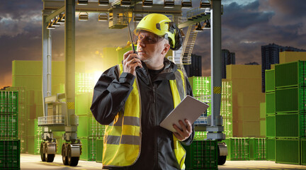 Port worker in safety gear with tablet and walkie-talkie supervising cargo operations among...