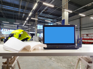 Workstation in industrial warehouse with open book, helmet, laptop and radio on table, ready for...