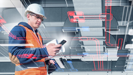 Engineer in helmet and safety vest uses smartphone and tablet to check smart HVAC system with...