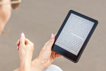 Woman reading e-book sitting on bench in city park (corrected).