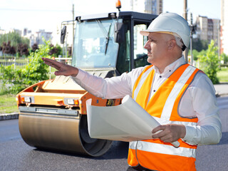 Man driver of asphalt paver. Road construction. Erection of asphalt sidewalks. Worker in orange...