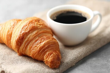 A freshly baked croissant placed next to a steaming cup of coffee on a linen cloth on a soft surface.
