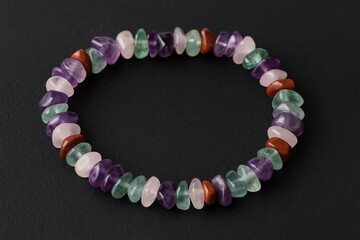 Detailed shot of a gemstone necklace featuring amethyst, fluorite, jasper, and rose quartz on a dark surface