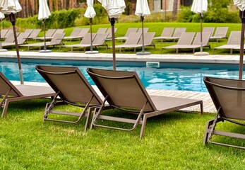 Relaxing summer scene with sun loungers by the pool in a green park with trees and grass