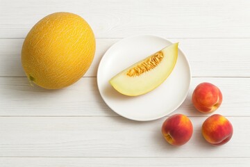 Arrangement featuring a ripe melon, a plate, and peaches on a white wooden surface