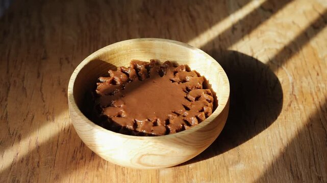 Finnish M&auml;mmi, a traditional rye pudding served in a wooden bowl, with a creamy texture and dark rich color, natural light on a wooden countertop, subtle shadows
