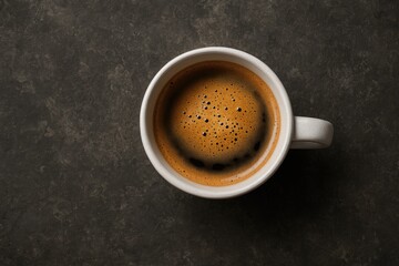 Aerial perspective of a dark ceramic mug filled with steaming black coffee topped with rich brown crema, resting on a textured concrete surface.