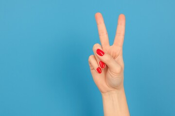 Woman's hand displaying the V sign with red nail polish against a blue backdrop with space for text