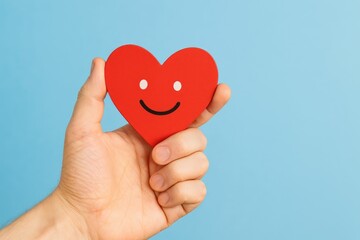 Fototapeta premium A person holding a vibrant red heart against a blue backdrop, symbolizing compassion and wellness.