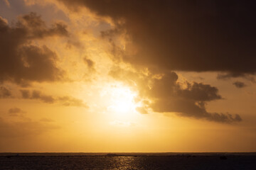 A golden sun setting over a tropical island reef featuring beautiful clouds in a dramatic glowing sky.