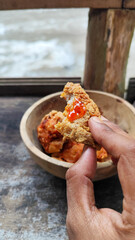 Tahu walik. Crispy browned tofu walik served in a natural wooden bowl with spicy chili sauce, with a blurry river flowing in the background. Menu at an outdoor cafe.