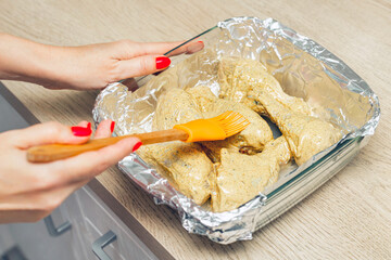 housewife prepares chicken legs for baking in the oven. woman spreads sauce on raw chicken legs....