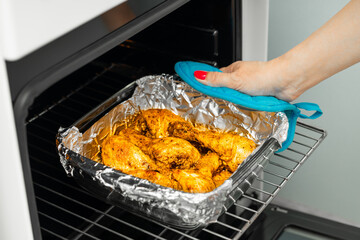 housewife takes fried chicken legs out of the oven. cooking chicken legs in the oven