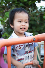 Close-up portrait of smiling boy having fun climbing toys in playground, 2 year old Asian child...
