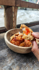 Tahu walik. Crispy browned tofu walik served in a natural wooden bowl with spicy chili sauce, with a blurry river flowing in the background. Menu at an outdoor cafe.