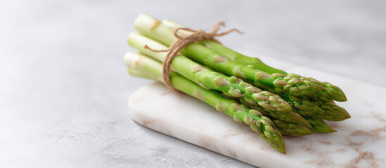 A bunch of fresh asparagus tied with twine rests on a marble cutting board. Healthy eating, fresh vegetables, cooking ingredient