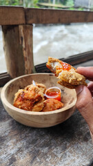 Tahu walik. Crispy browned tofu walik served in a natural wooden bowl with spicy chili sauce, with a blurry river flowing in the background. Menu at an outdoor cafe.