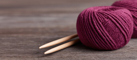A ball of burgundy yarn with wooden knitting needles rests on a wooden surface. Crafting, knitting, hobby, yarn