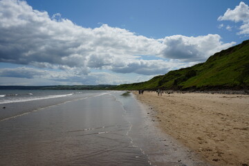Stunning coastal landscape with sandy beach, rocky cliffs, and walkers enjoying the view at Filey,...