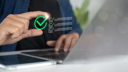 Close-up of hand holding digital green check mark with online task list icon, representing business success and digital technology.