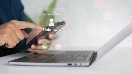 Close-up of a hand holding a smartphone showing an unknown incoming call warning with alert icons, representing a scam call, phishing threat, and cybersecurity risk.