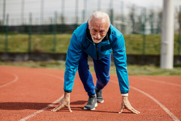 Front view of old athlete in starting line on stadium preparing for running.