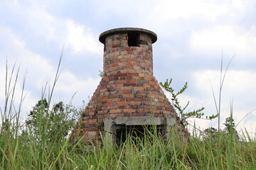 Old brick incinerator structure in overgrown grassy field