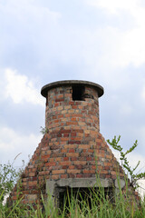 Old brick incinerator structure in overgrown grassy field