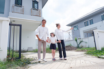 Father and mother are hugging their smiling daughter as they stand in front of the house.