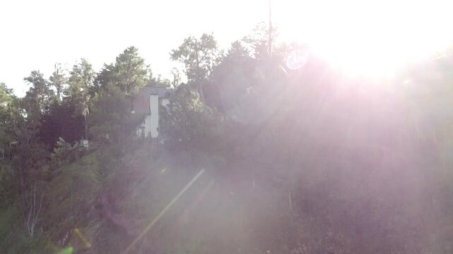 Aerial drone shot rising into the sky with the sun directly ahead, revealing a mountainous landscape at dawn in Constanza. Serene early morning light and natural scenery create a peaceful atmosphere.