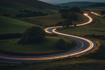 Winding curvy rural road with light trail from headlights leading through British countryside.