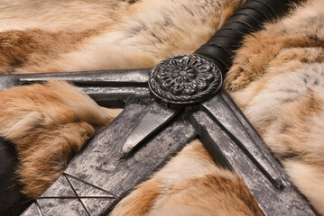 Old long medieval two handed knight warrior sword and animal beast fur on ancient table background.