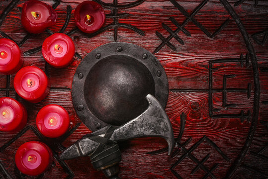 Medieval Viking axe and warrior red shield in the light of burning candles on old warrior table close up background.