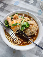 Bakso. A complete bowl of meatballs with yellow noodles, crispy fried dumplings and fresh green vegetables served with delicious, rich sauce on the table.