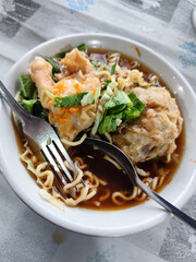 Bakso. A complete bowl of meatballs with yellow noodles, crispy fried dumplings and fresh green vegetables served with delicious, rich sauce on the table.