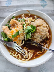 Bakso. A complete bowl of meatballs with yellow noodles, crispy fried dumplings and fresh green vegetables served with delicious, rich sauce on the table.