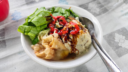 Bakso. A complete bowl of meatballs with yellow noodles, crispy fried dumplings and fresh green vegetables served with delicious, rich sauce on the table.