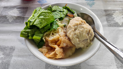 Bakso. A complete bowl of meatballs with yellow noodles, crispy fried dumplings and fresh green vegetables served with delicious, rich sauce on the table.