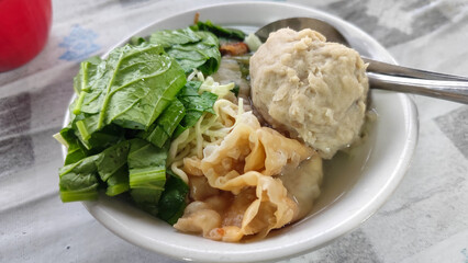 Bakso. A complete bowl of meatballs with yellow noodles, crispy fried dumplings and fresh green vegetables served with delicious, rich sauce on the table.