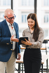 Smiling businesswoman showing digital tablet to senior businessman in modern office, teamwork and...