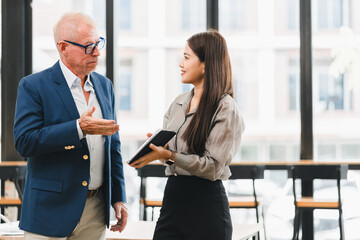 Businessman and businesswoman discussing project in modern office, professional teamwork, collaboration, and communication, both standing and holding digital tablet, bright window background