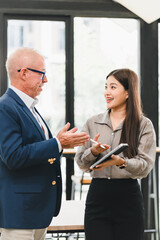 Businessman and businesswoman discussing project in modern office, smiling and holding digital tablet, teamwork and collaboration concept