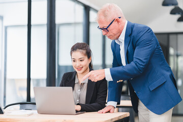 Fototapeta premium Businesswoman and senior businessman working together office desk, discussing project laptop with teamwork and mentoring, modern workplace environment, professional collaboration, positive mood