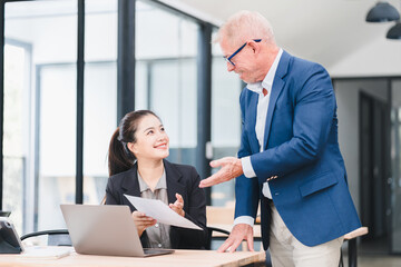 Businesswoman and senior businessman discussing document at modern office desk, teamwork and...