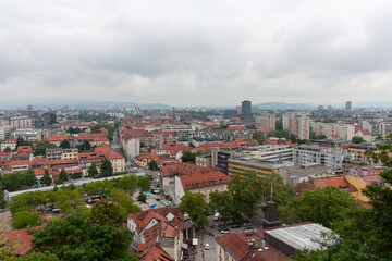 An expansive elevated view captures the cityscape of Ljubljana, on a cloudy day. Red-tiled rooftops...