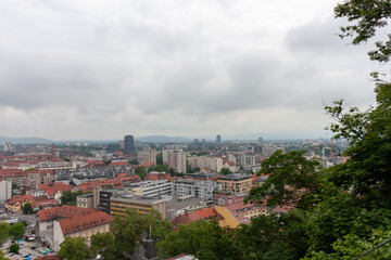 An expansive elevated view captures the cityscape of Ljubljana, on a cloudy day. Red-tiled rooftops...