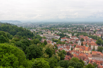 An expansive elevated view captures the cityscape of Ljubljana, on a cloudy day. Red-tiled rooftops...