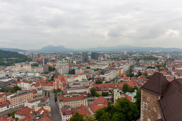 An expansive elevated view captures the cityscape of Ljubljana, on a cloudy day. Red-tiled rooftops...