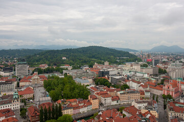 An expansive elevated view captures the cityscape of Ljubljana, on a cloudy day. Red-tiled rooftops...