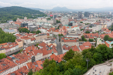 An expansive elevated view captures the cityscape of Ljubljana, on a cloudy day. Red-tiled rooftops...